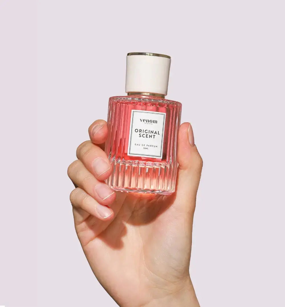 Hand holding a clear, ribbed bottle of pink perfume labeled 'Venom Original Scent.'
