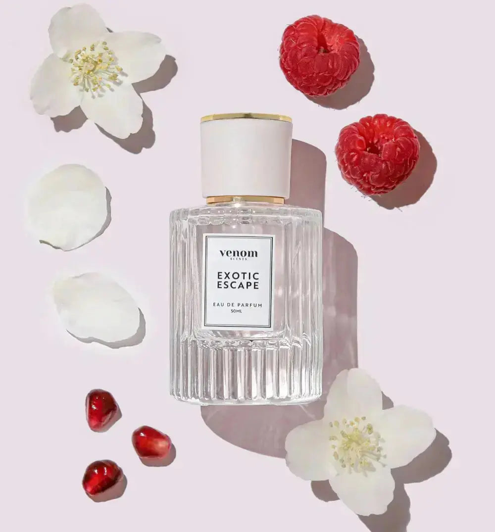 Perfume bottle surrounded by white flowers, raspberries, and pomegranate seeds.