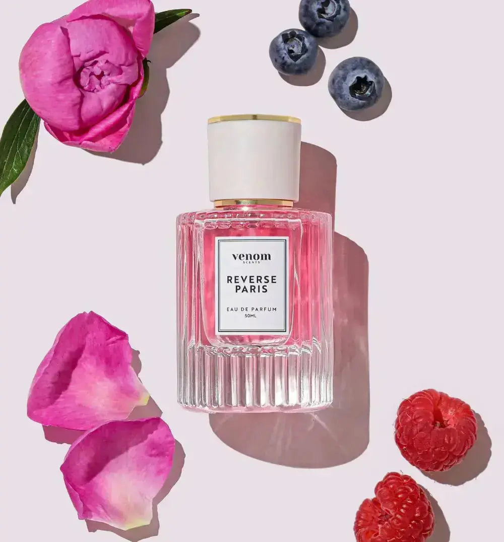 Perfume bottle with pink liquid, surrounded by flowers, raspberries, and blueberries.